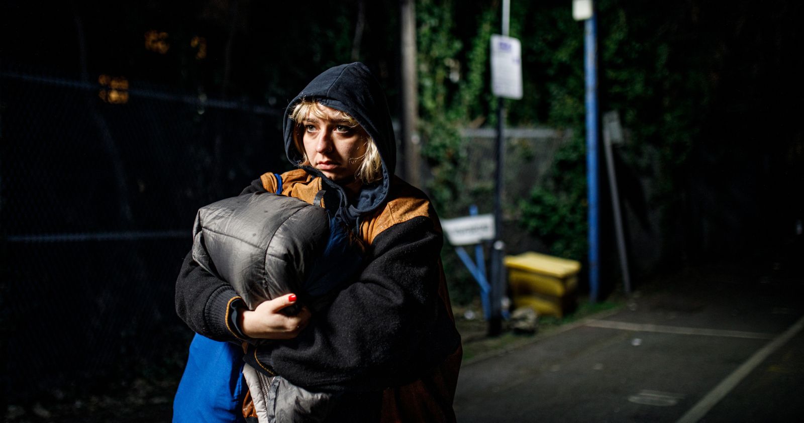 Image: a rough sleeper holding a sleeping bag at night